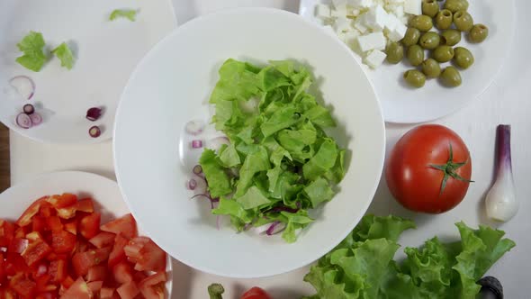 Adding Feta Cheese Cubes Into a Greek Salad on the Table in