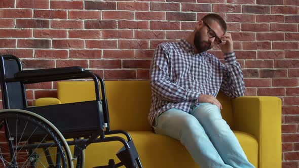 Person with Disabilities is Sitting on Sofa and Thinking with Serious Look Front View alt