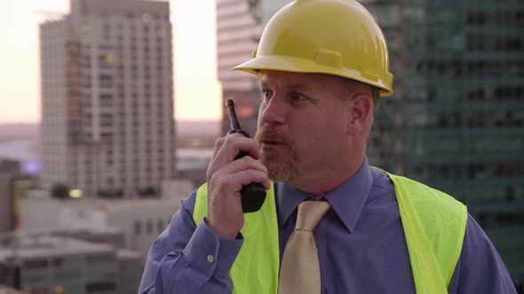 Construction manager on rooftop talking on walkie talkie