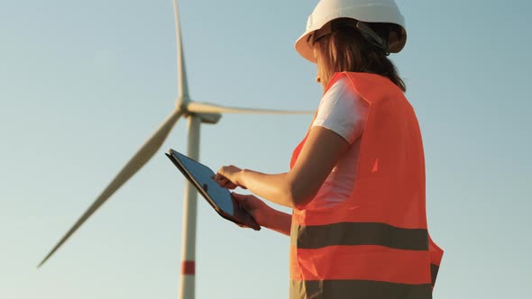 Female an Engineer in a Helmet and an Orange Vest Controls the Operation of a Wind Turbine Using a alt