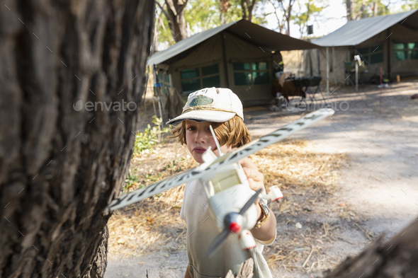Young boy in tented safari camp holding a model airplane.