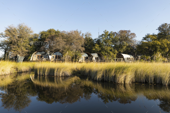 Small group of permanent safari camp tents by a waterway.