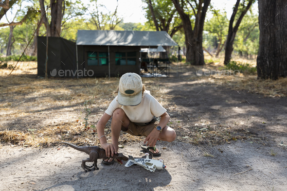 Young boy in tented safari camp playing with a toy dinosaur and a toy aeroplane.