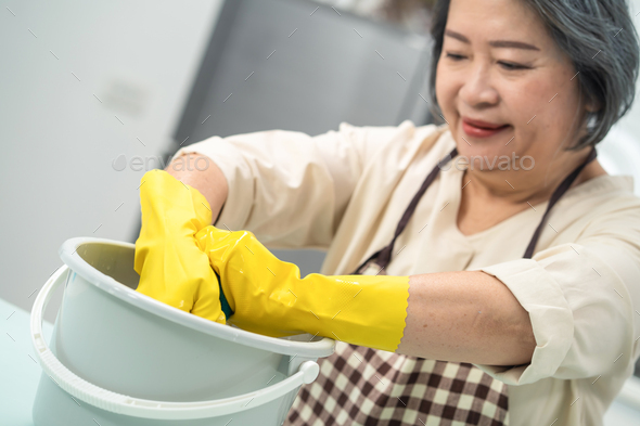 Asian young aged housewife twisting wet rag to clean the kitchen counter at home.