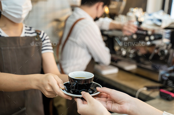Asian Barista waiter handing a cup of hot coffee to customer at cafe.