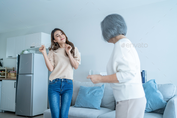 Asian funny senior old mom and daughter dance together in living room.