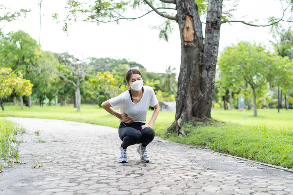 Asian sport woman wear mask feels pain on stomach after run on street.