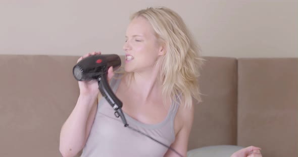 Woman holding hair dryer and singing in bedroom