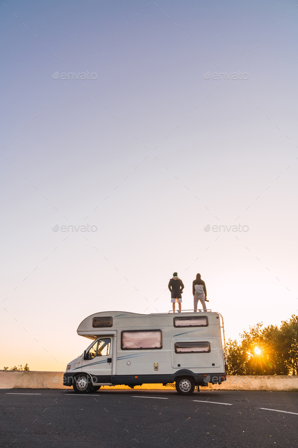 Men on camper van on road and blue sky at sunset