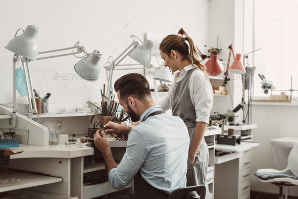 Master and apprentice. Young male assistant and female jeweler are working together at jewelry