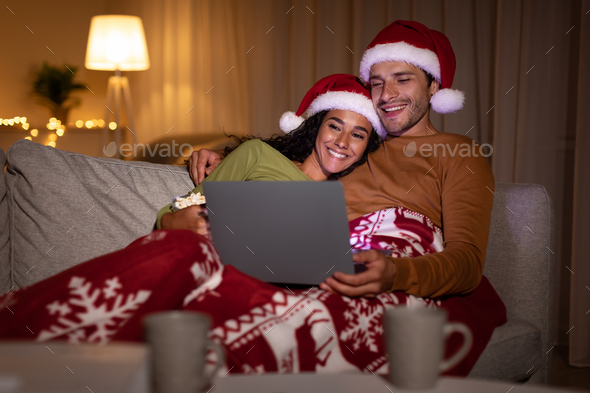 Happy Couple Watching Christmas Films Online On Laptop At Home