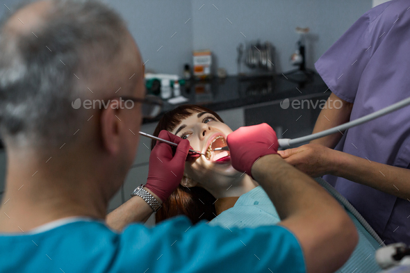 Medical dentist team in modern dental office doing treatment of tooth for female