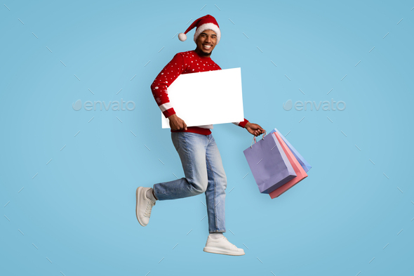 Happy black guy with blank placard shopping while xmas sales