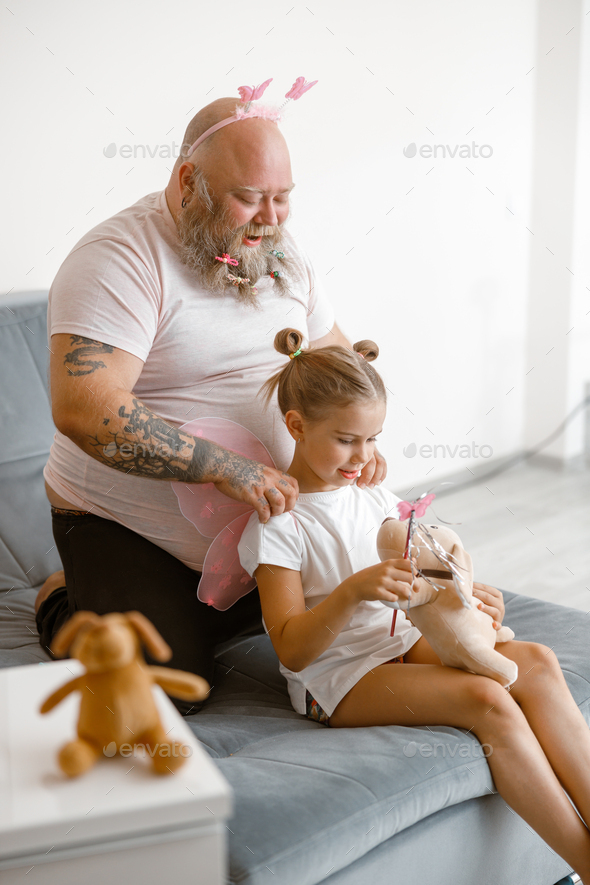 Funny daddy does massage to little girl holding toy dog and magic stick in living room