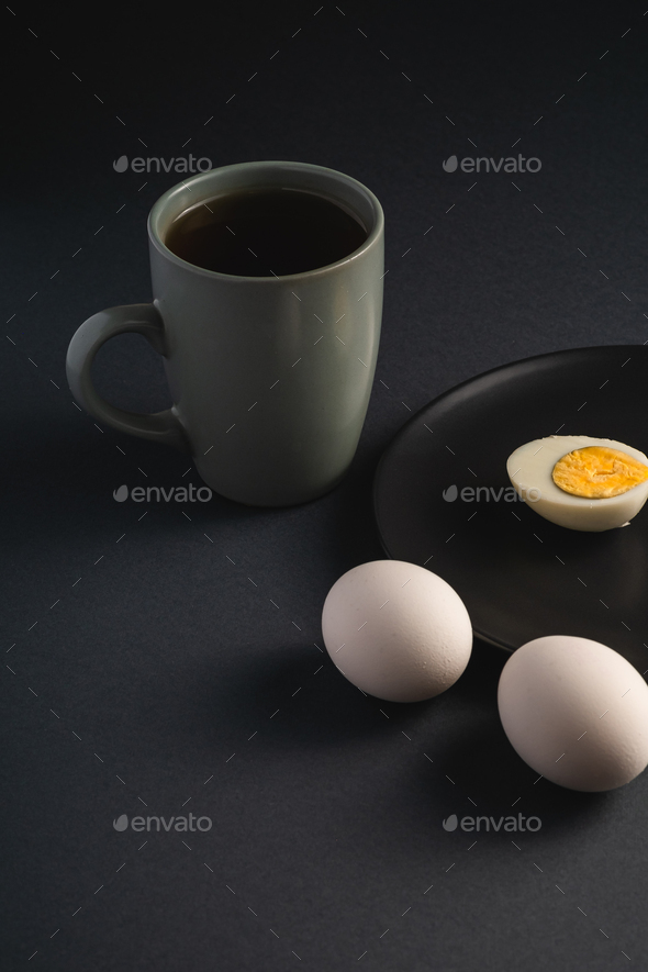 Boiled half egg with yolk in black plate near to white eggs and cup of tea