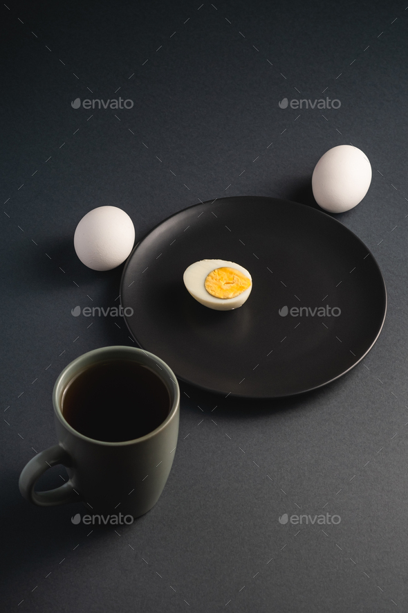 Boiled half egg with yolk in black plate near to white eggs and cup of tea