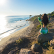 Attractive young woman sitting on a cliff by the beach looking at the ocean - PhotoDune Item for Sale