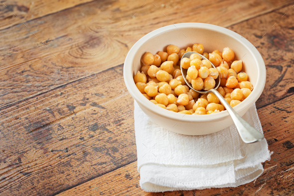Cooked chickpeas in white bowl on wooden background. Spilled chickpeas.