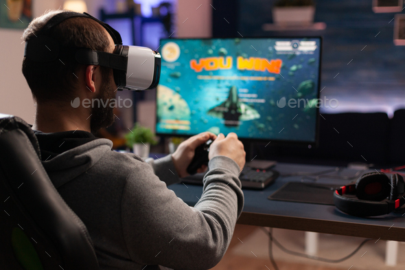 Person playing video games with controller on computer. Player using  joystick and wearing headphones to play online game on monitor. Modern man  using gaming equipment to have fun. Stock Photo