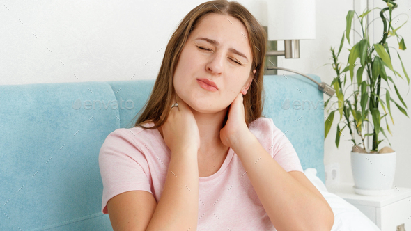 Portrait of young woman suffering from pain in neck massaging aching muscles - Stock Photo - Images