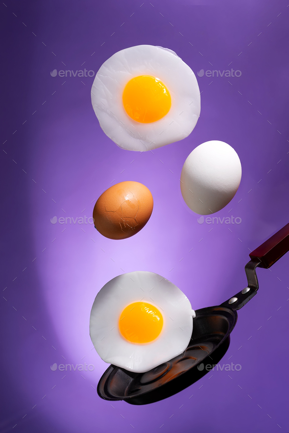 whole and fried eggs above a frying pan float in the air on a violet
