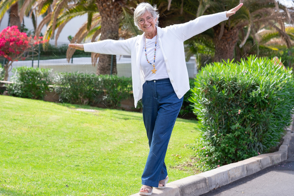 Happy senior woman walks on the curb with her arms outstretched to keep balance.