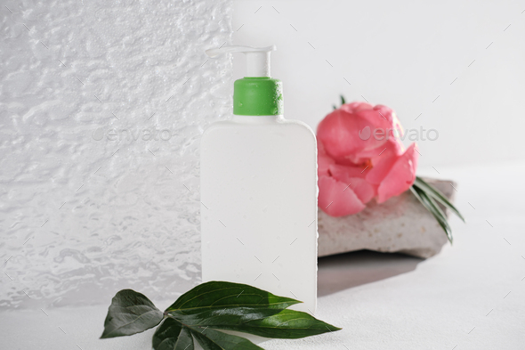 white cosmetic bottle with pump next to textured acrylic glass door and peony flower.