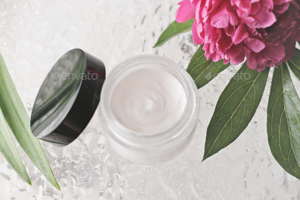 white cosmetic face cream in a glass bottle with black lid. peony flower and shower door.
