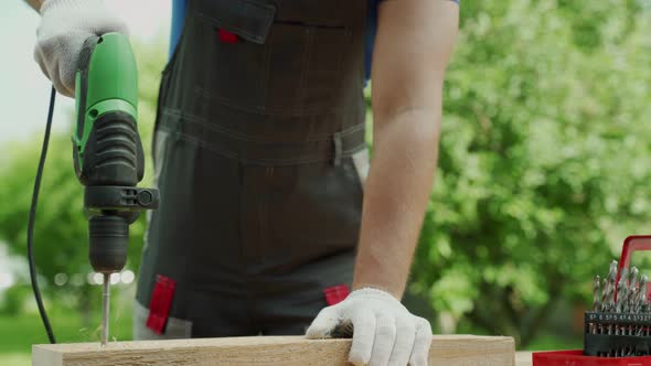 Close Up Hand of Carpenter Drills Wood a Hole with an Electrical Drill alt