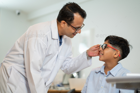 Optical staff or ophthalmologist touch glasses leg that glasses is wearing by Indian boy