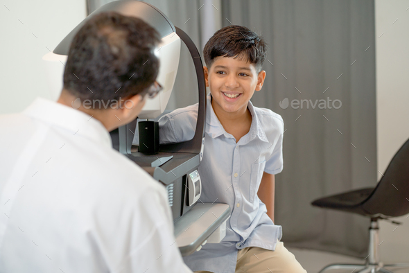 Indian boy look to optical staff or ophthalmologist during the process of using machine