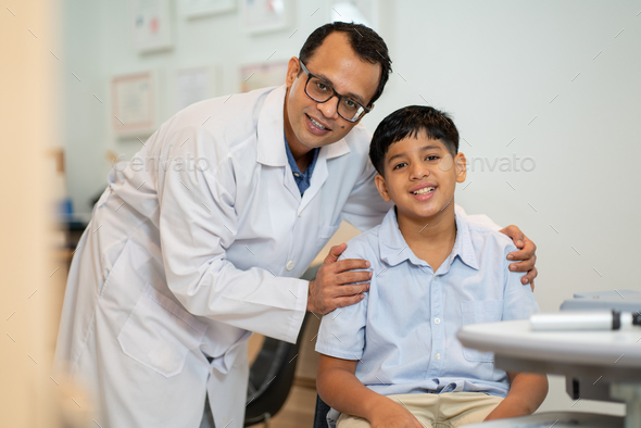 Optical staff or ophthalmologist hold shoulder of Indian boy and smiling with look at camera