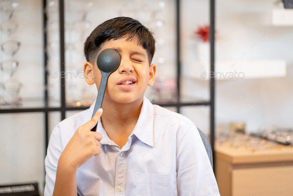 Indian boy has fun with use optical testing tool close his eye in optical shop.