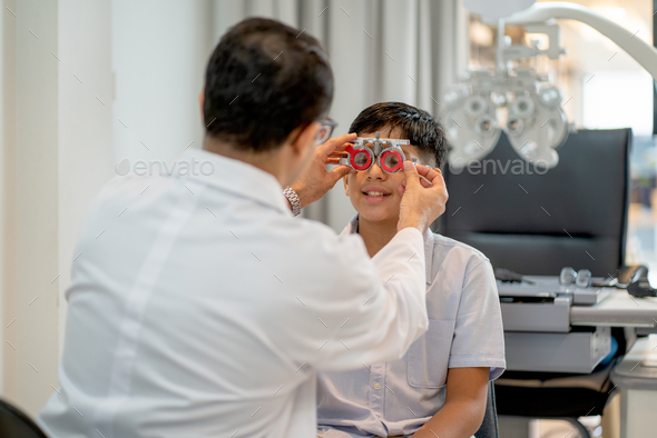Optical staff or ophthalmologist adjust special glasses for testing eyesight of Indian boy