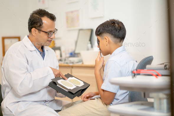 Ophthalmologist or optical staff use book of color blindness test with Indian boy