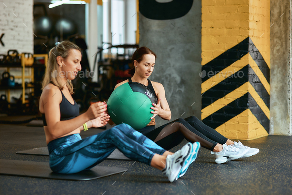 Staying active. Two young caucasian athletic women in sportswear exercising with fitness ball at gym