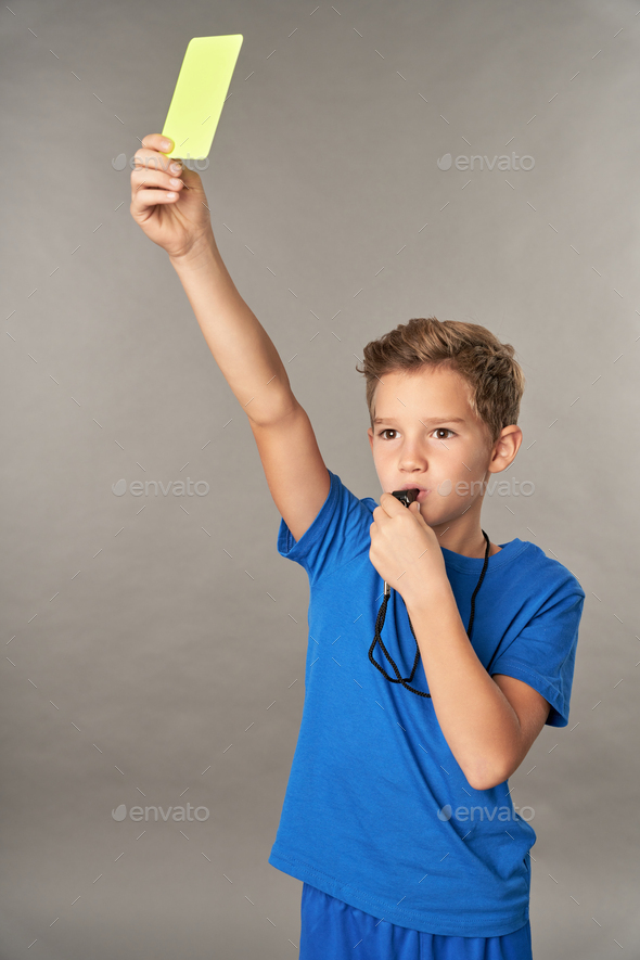 Cute boy holding yellow card and whistling in whistle