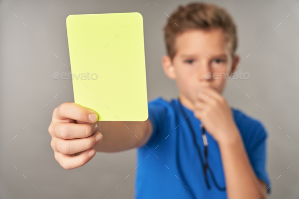 Little boy referee holding yellow card and whistling in whistle