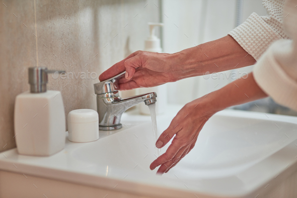 Female hands turning on water from basin mixer tap