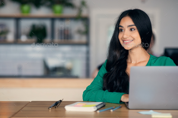 Excited middle eastern young woman working on laptop, cafe interior