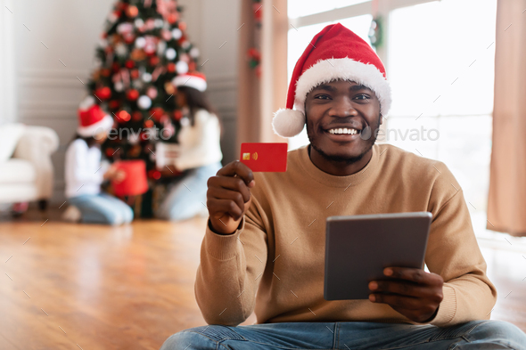 Xmas Shopping. Smiling black guy using tablet showing credit card