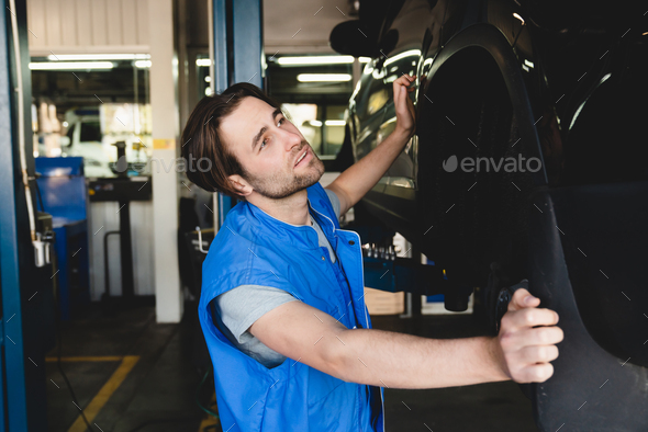 MOT. Vehicle inspection. Young handsome car auto mechanic technician repairing fixing car tires