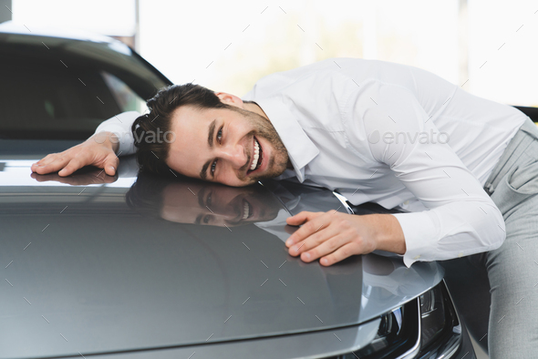 Businessman hugging his new car, feeling excited after buying expensive auto at auto dealer shop