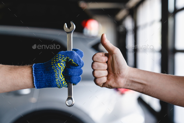 Wrench in technician mechanic hands while male hand showing thumb up. MOT. Vehicle inspection