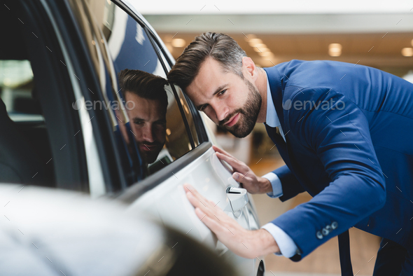 Businessman checking new car options at dealer shop before buying it, dreaming about automobile