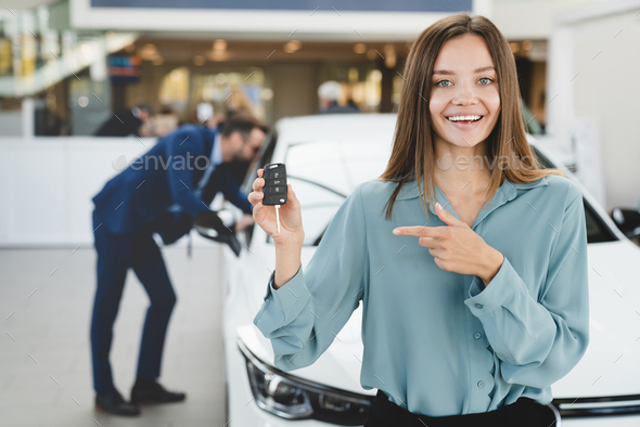 Businesswoman pointing at car keys after buying purchasing expensive car at automobile dealer shop