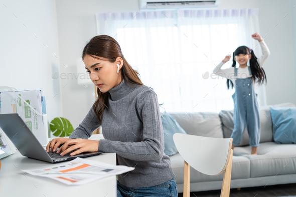 Asian business woman work at home with young kid daughter play around.
