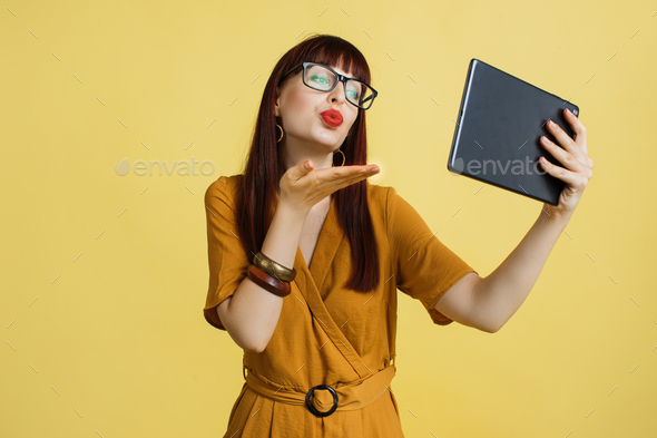 girl in spectacles and yellow dress, sending air kiss during video call