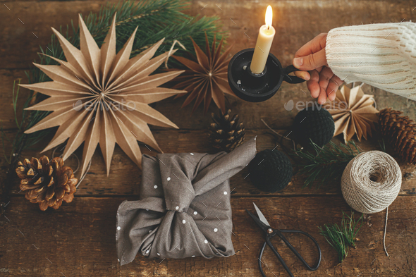 Stylish christmas gift wrapped in fabric on rustic table with scissors,  paper star, candle.Furoshiki Stock Photo by Sonyachny