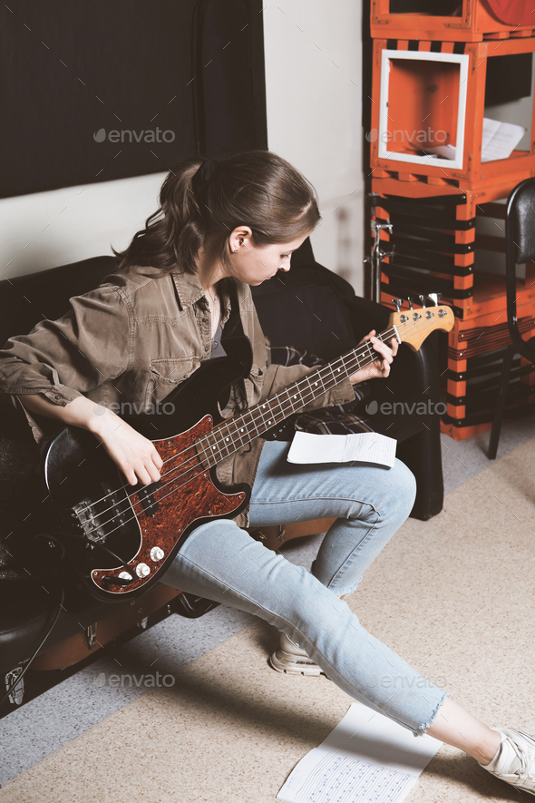 young woman playing bass guitar and looking at chords notes. rehearsal room.